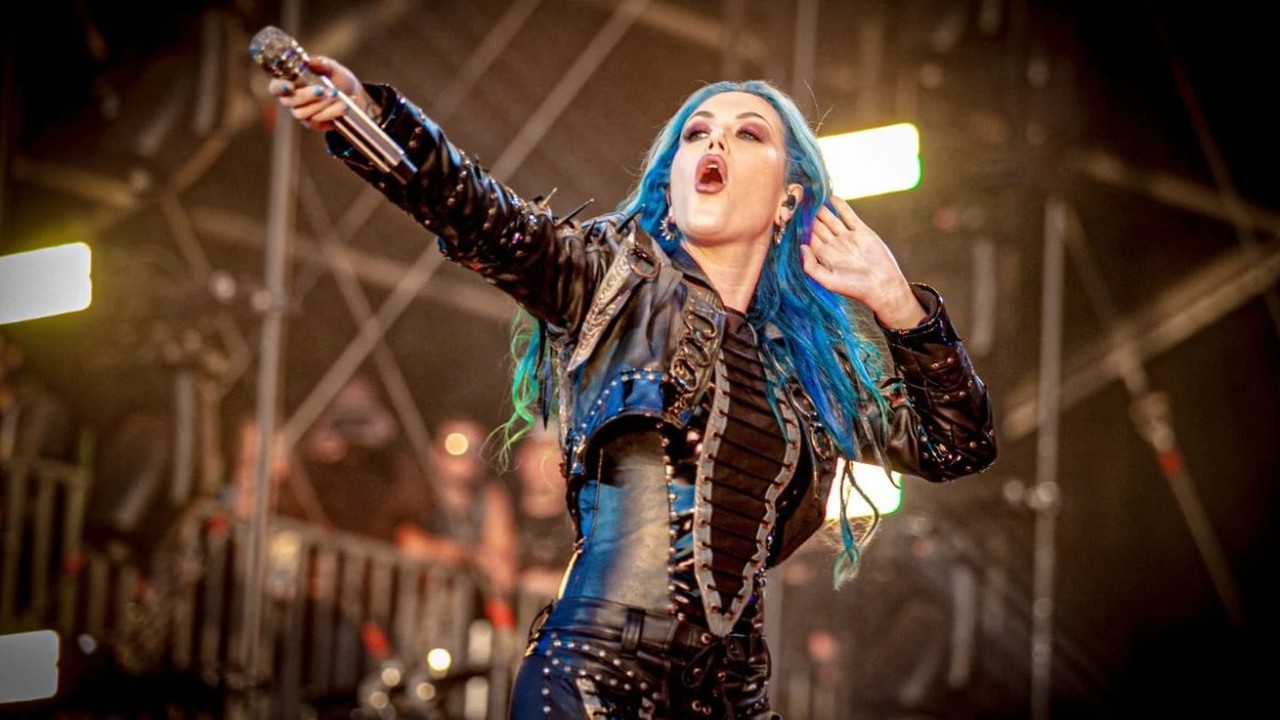 Alissa White-Gluz en vivo, con el brazo en alto y el micrófono